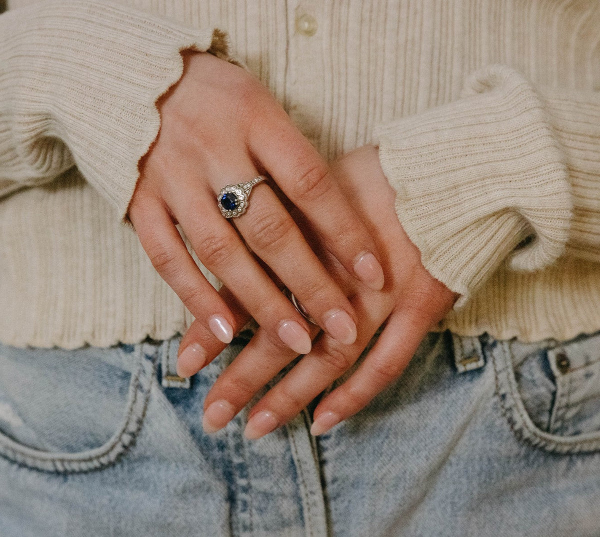 Close-up of hands with a ring, wearing a beige sweater and blue jeans.